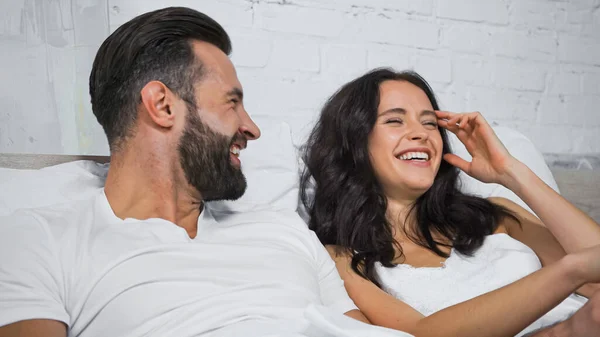 Aufgeregte Frau lacht neben glücklichem Freund im heimischen Bett — Stockfoto