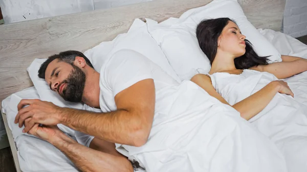 Bearded man messaging on smartphone while lying near sleeping girlfriend — Stock Photo