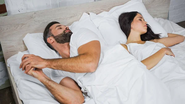 Hombre con teléfono móvil mirando a su novia durmiendo cerca en la cama - foto de stock
