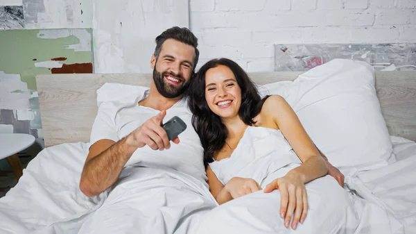 Cheerful man pointing with finger while watching tv with girlfriend in bedroom — Stock Photo