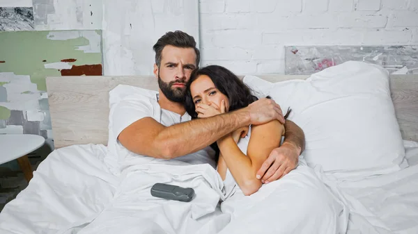 Preocupado casal abraçando enquanto assiste filme na cama — Fotografia de Stock