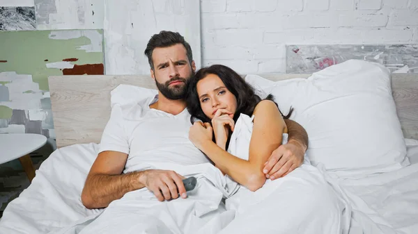 Tense man embracing worried woman while watching tv in bedroom — Stock Photo
