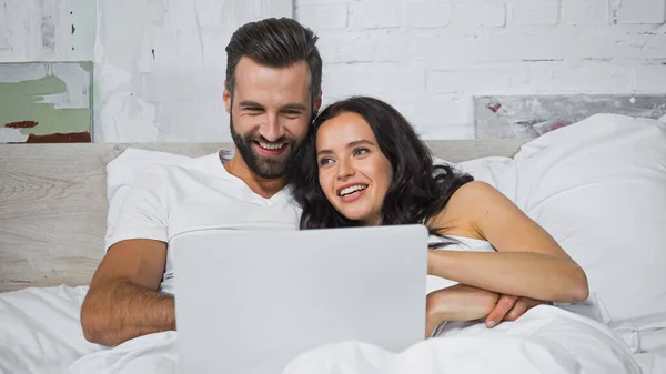 Cheerful young couple watching movie on computer in bedroom — Stock Photo