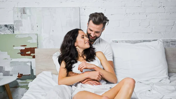 Бородатий чоловік обіймає щасливу дівчину брюнетки в спальні — стокове фото