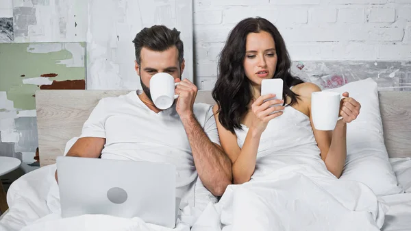 Young couple drinking coffee and using gadgets in bedroom — Stock Photo