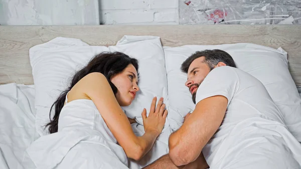 Brunette woman and bearded man looking at each other while lying in bed — Stock Photo