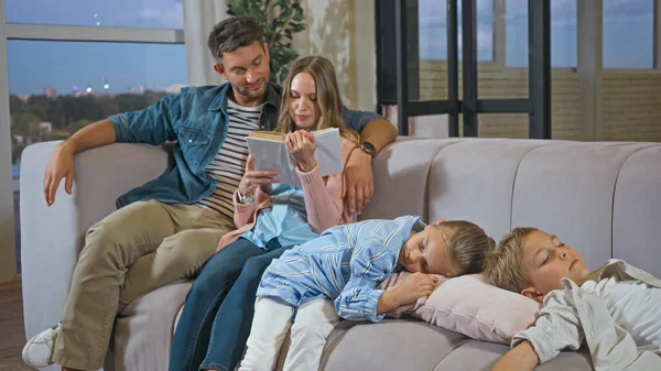 Enfants dormant près des parents avec livre sur canapé — Photo de stock