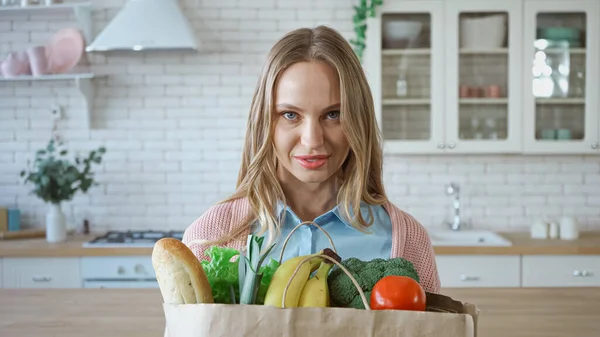 Mulher com comida em saco de papel sorrindo para a câmera na cozinha — Fotografia de Stock