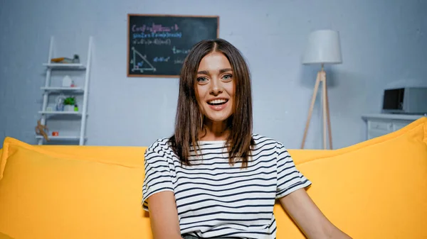 Fröhliche Frau blickt auf gelbem Sofa in die Kamera — Stockfoto