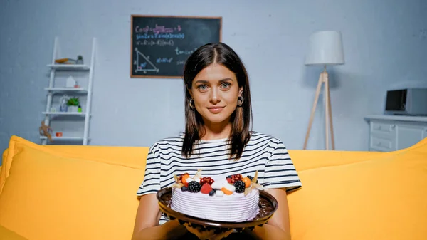 Young woman holding tasty cake on couch — Stock Photo