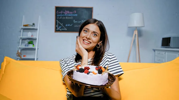 Donna allegra guardando la fotocamera mentre tiene la torta con bacche — Foto stock