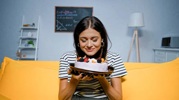 Молодая женщина держит вкусный торт с закрытыми глазами в гостиной — стоковое фото