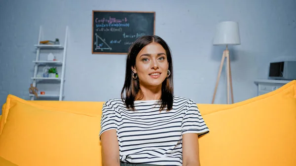 Положительная женщина в полосатой футболке смотрит в камеру дома — стоковое фото