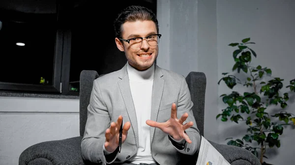 Улыбающийся бизнесмен с ручкой разговаривает перед камерой возле бумаги во время видеозвонка — стоковое фото