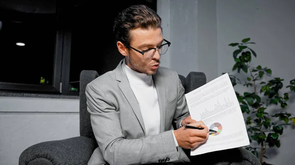 Businessman in suit showing chart on document during video call in office — Stock Photo