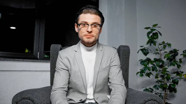 Young manager in eyeglasses looking at camera while sitting on armchair — Stock Photo
