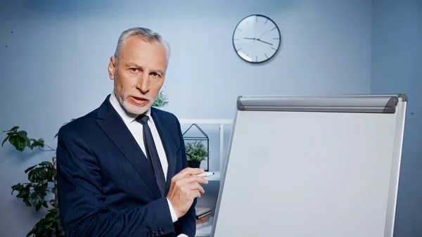 Businessman with marker standing near flipchart in office — Stock Photo