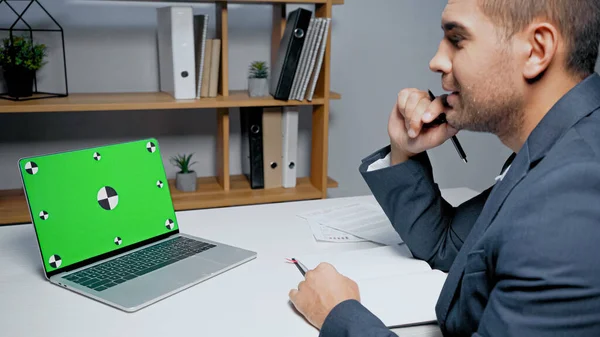 Laptop com chave chroma perto de empresário com caneta e notebook em primeiro plano desfocado — Fotografia de Stock