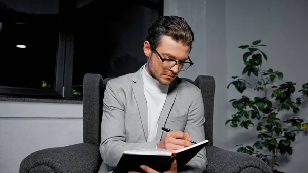 Young businessman writing on notebook on armchair in office — Stock Photo