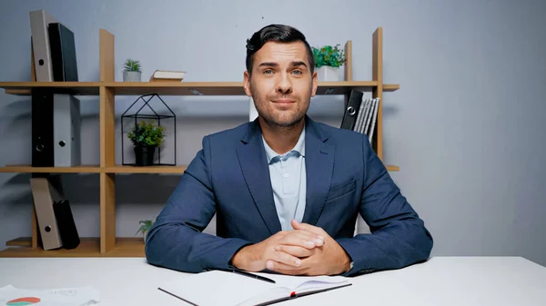 Manager im Anzug sitzt neben Copybook und Dokumenten im verschwommenen Vordergrund — Stockfoto