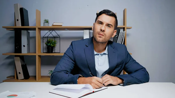 Фокусований бізнесмен тримає ручку біля копії книги в офісі — стокове фото