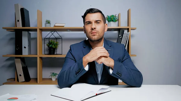 Geschäftsmann blickt auf Kamera neben Notizbuch auf Tisch — Stockfoto