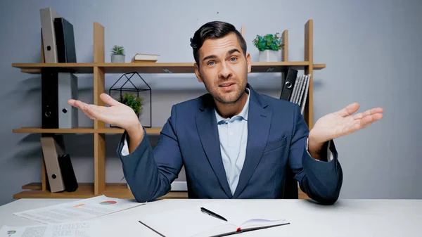 Улыбающийся бизнесмен, показывающий руками во время видеозвонка в офисе — стоковое фото