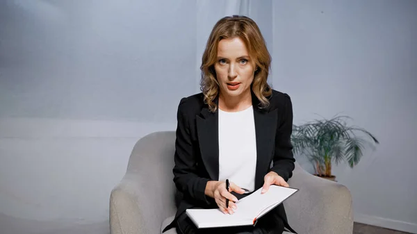 Adult businesswoman talking at camera and holding notebook and pen — Stock Photo