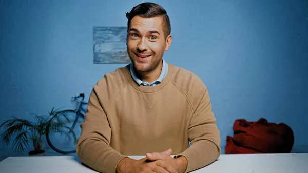 Улыбающийся мужчина в коричневом свитере смотрит в камеру дома — стоковое фото