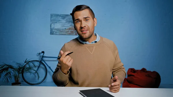 Homem com caneta e caderno conversando na câmera durante videochamada em casa — Fotografia de Stock