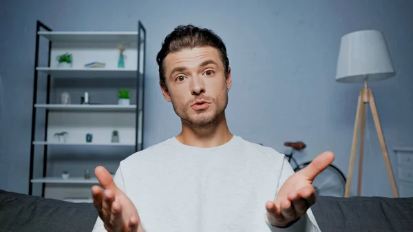 Parler homme pointant avec les mains à la caméra pendant le chat vidéo à la maison — Photo de stock