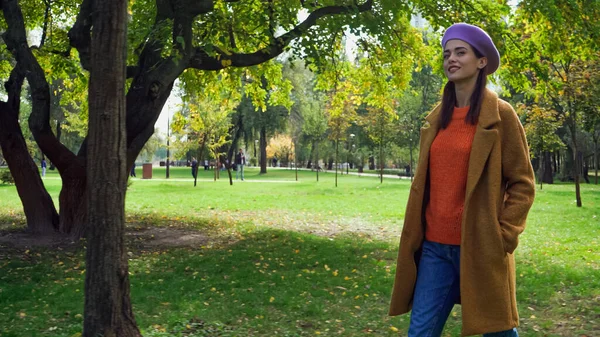 Mujer feliz en elegante traje de otoño paseando en el parque con la mano en el bolsillo - foto de stock