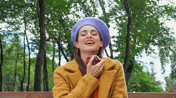 Excité femme rire avec les yeux fermés tout en tenant pomme mûre dans le parc — Photo de stock