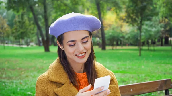 Alegre mujer de moda charlando en el teléfono inteligente en el parque de otoño - foto de stock