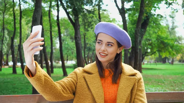 Femme heureuse en tenue d'automne prendre selfie sur téléphone mobile dans le parc — Photo de stock