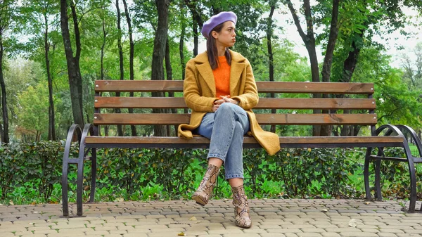 Displeased stylish woman sitting on bench in park and looking away — Stock Photo