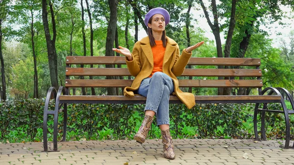 Mujer ofendida mostrando gesto de encogimiento mientras espera en el banco en el parque - foto de stock