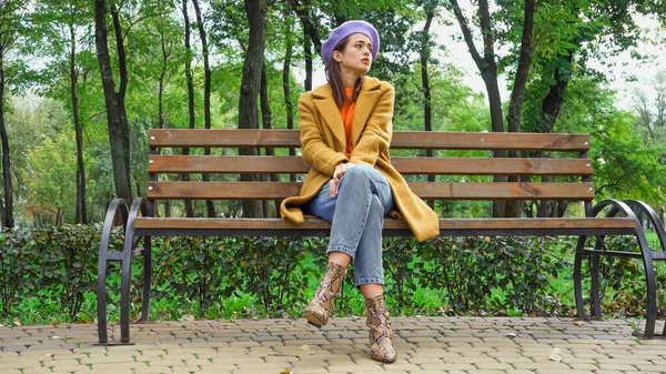 Femme triste regardant loin tout en étant assis sur le banc dans le parc d'automne — Photo de stock