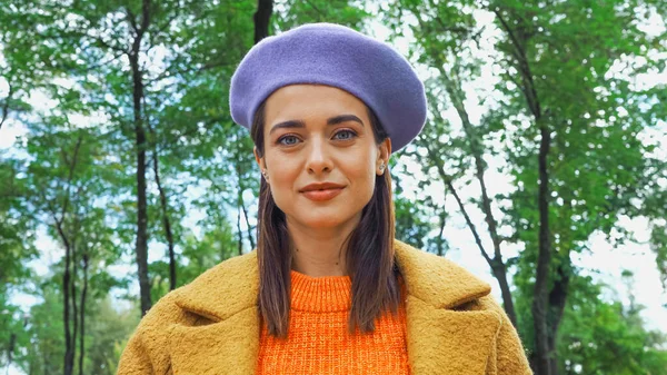 Giovane donna in berretto alla moda guardando la fotocamera nel parco — Foto stock
