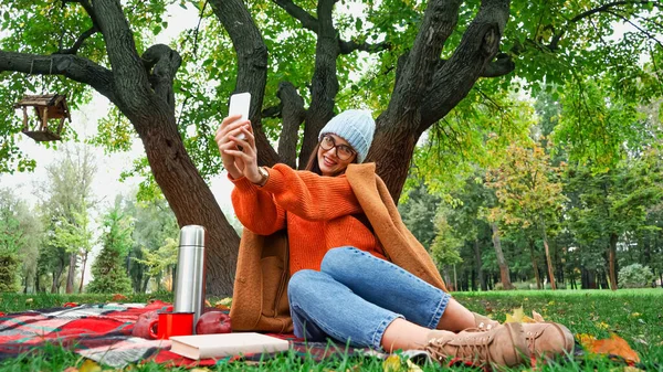 Jeune femme heureuse prenant selfie sur smartphone pendant le pique-nique dans le parc d'automne — Photo de stock