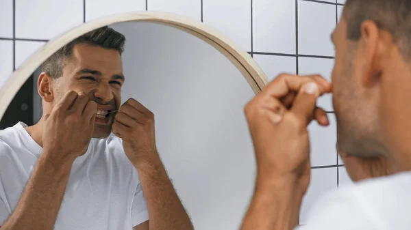Young man cleaning teeth with dental floss in bathroom — Stock Photo