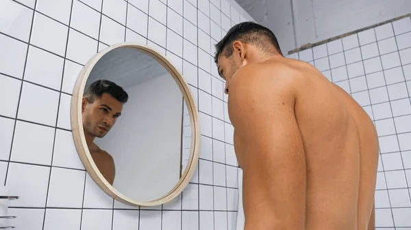 Vue à angle bas de jeune homme torse nu regardant miroir dans la salle de bain — Photo de stock