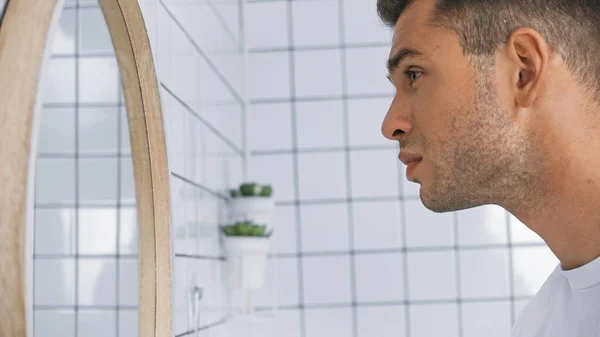 Side view of man with perfect skin looking at mirror in bathroom — Stock Photo