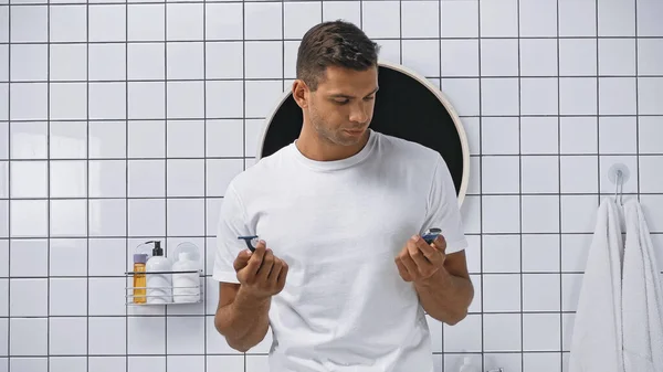 Чоловік у білій футболці тримає запобіжник і електричну бритву у ванній кімнаті — стокове фото