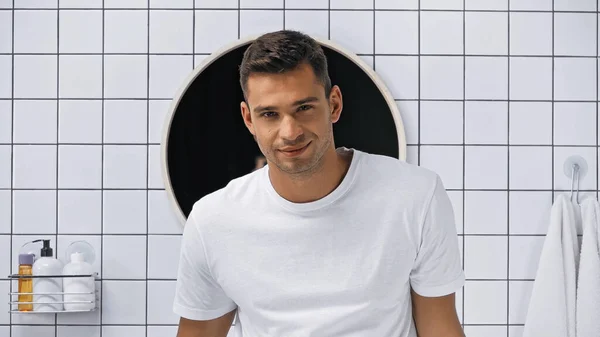 Happy man in white t-shirt looking at camera in bathroom — Stock Photo