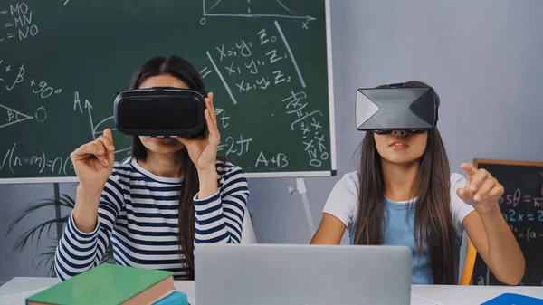 Chica jugando y apuntando con el dedo cerca de la madre en vr auriculares en casa - foto de stock