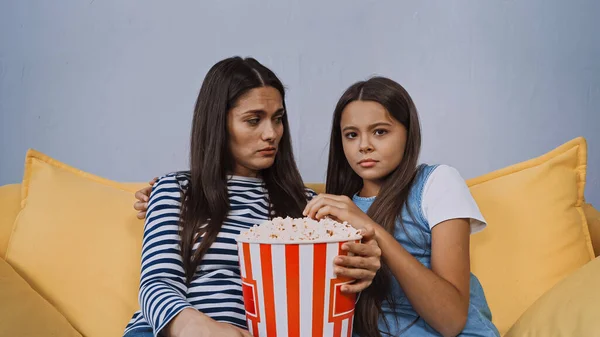 Madre e hija viendo película cerca de cubo con palomitas de maíz sabrosas - foto de stock