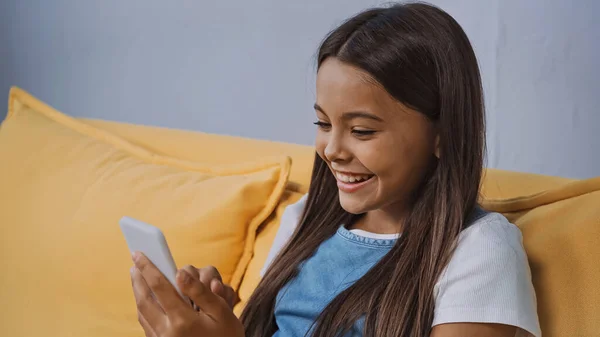 Menina feliz usando smartphone e sorrindo na sala de estar — Fotografia de Stock