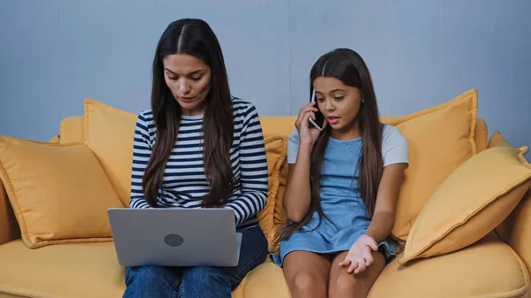 Mother using laptop while kid talking on smartphone in living room — Stock Photo