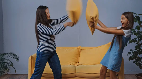 Happy mother and excited daughter pillow fighting in living room — Stock Photo
